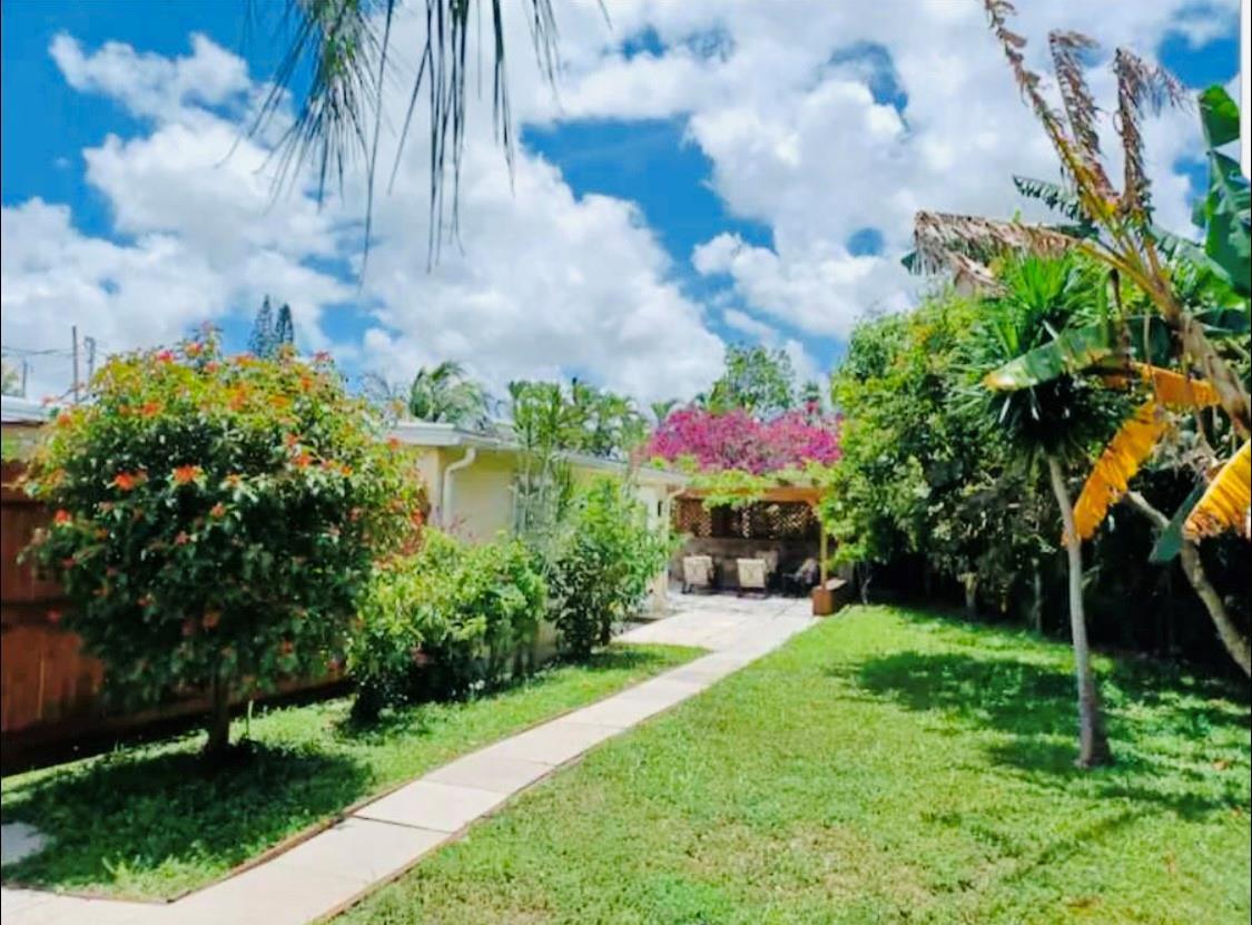 A grassy backyard features a stone walkway leading to a covered patio area with seating — 279 Hach Lane, West Palm Beach FL 33415, WEST PALM BEACH, FL