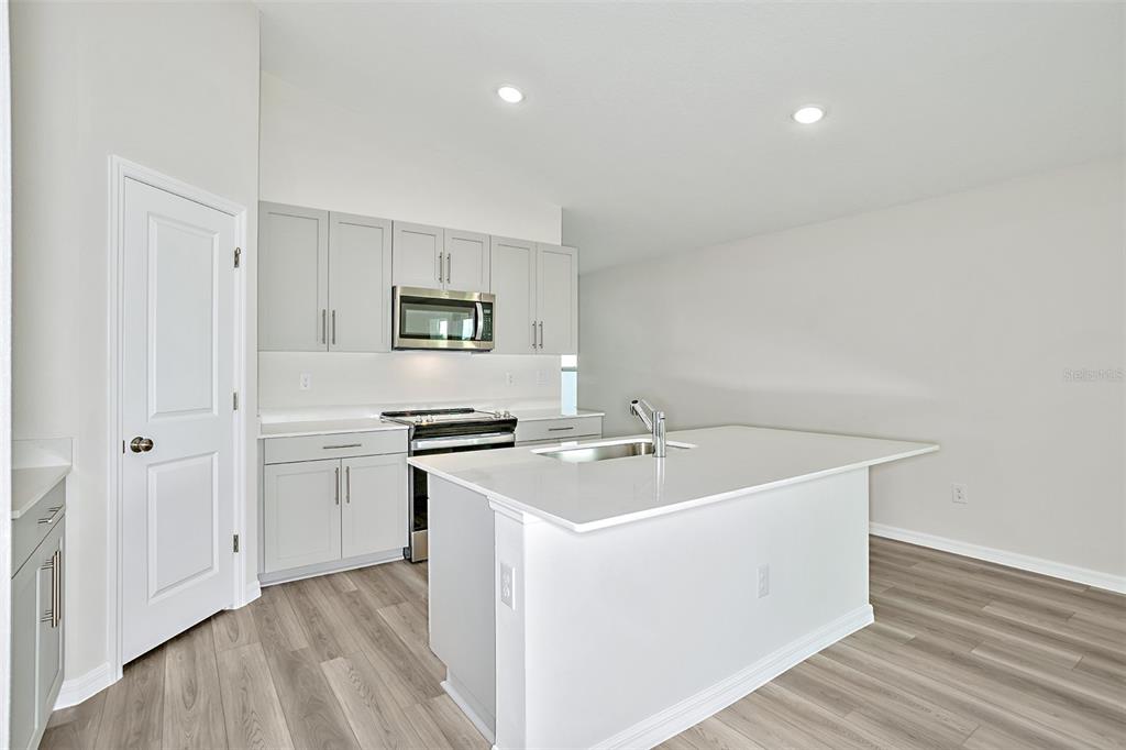 A modern kitchen features light gray cabinets, stainless steel appliances, and a white quartz island — 15204 MAUDE LANDING LOOP, WIMAUMA, FL