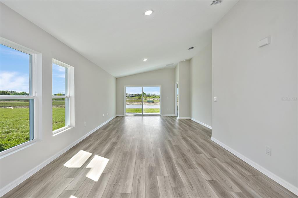 An empty room with light wood-look flooring, white walls, recessed lighting, and sliding glass doors — 15204 MAUDE LANDING LOOP, WIMAUMA, FL