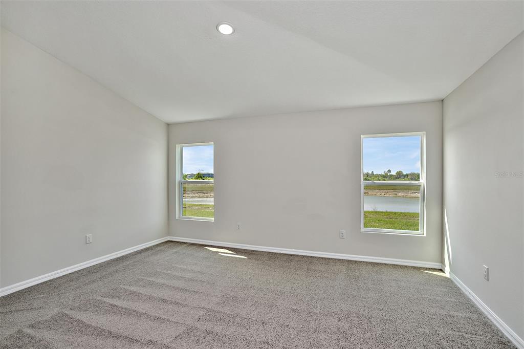 An empty bedroom with gray carpet, light walls, and two windows overlooking a pond — 15204 MAUDE LANDING LOOP, WIMAUMA, FL