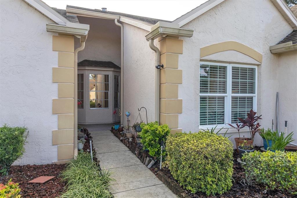 A concrete walkway leads to the recessed front entrance of a stucco house with quoins — 11436 VERSAILLES LANE, PORT RICHEY, FL