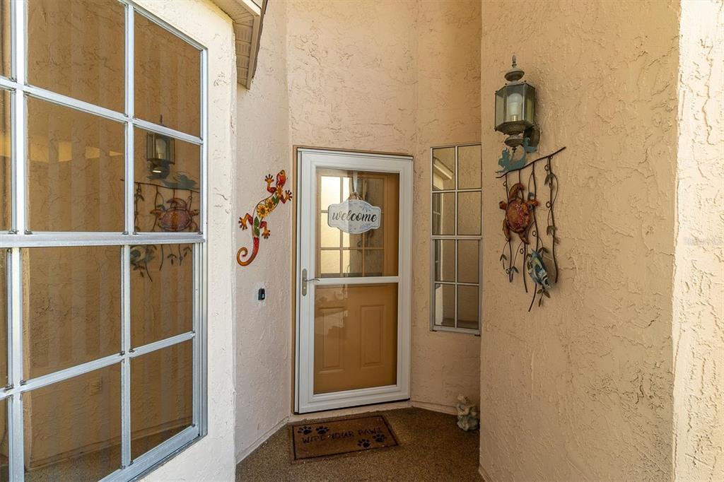An exterior entryway features a tan door with a welcome sign and decorative wall art — 11436 VERSAILLES LANE, PORT RICHEY, FL