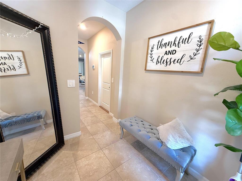 A hallway features tile flooring, an arched entryway, a tufted bench, and wall decor — 6549 SERENITY FALL LANE, SARASOTA, FL