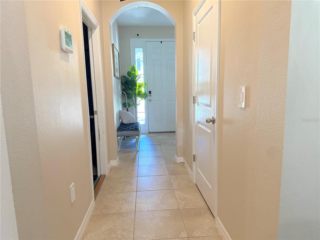 A tiled hallway leads to a white front door with an arched entryway — 6549 SERENITY FALL LANE, SARASOTA, FL