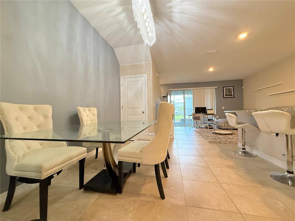 A dining area with a glass table and tufted chairs opens into a living space — 6549 SERENITY FALL LANE, SARASOTA, FL