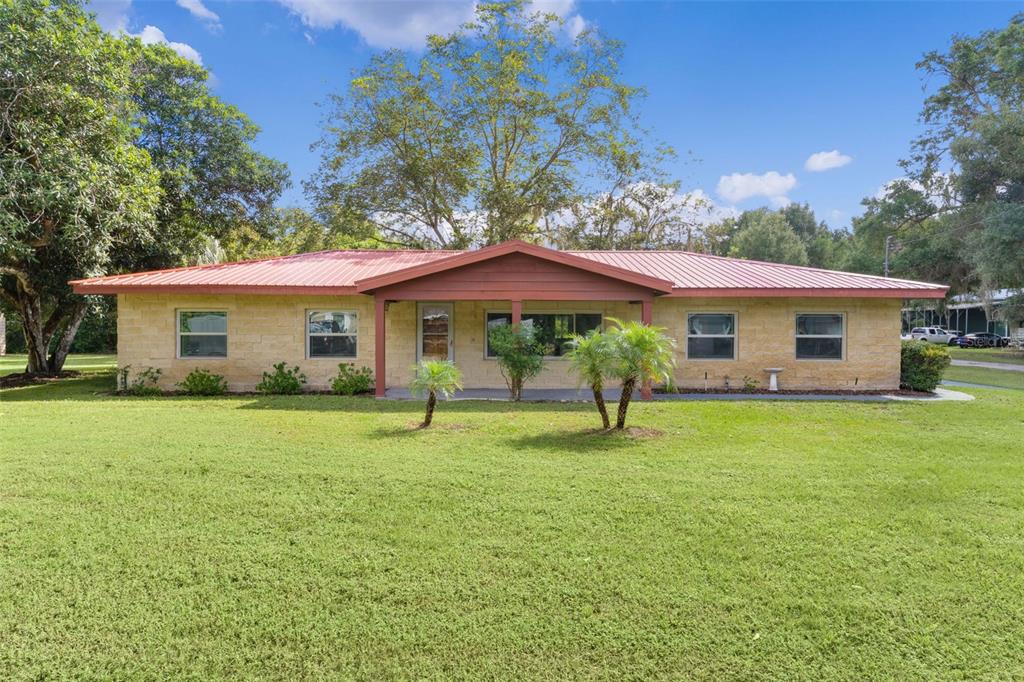 A single-story house with a stone facade and a red metal roof sits on grass — 14635 SE 28TH COURT, SUMMERFIELD, FL
