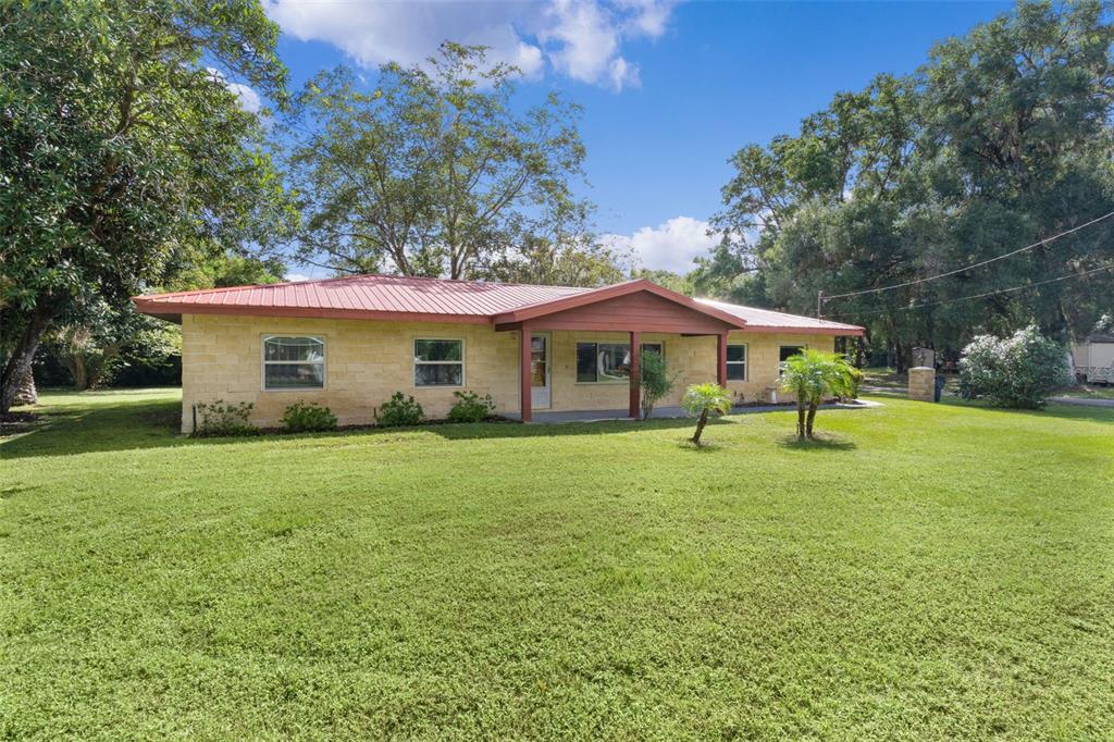A single-story house with a tan stone exterior and a red metal roof — 14635 SE 28TH COURT, SUMMERFIELD, FL