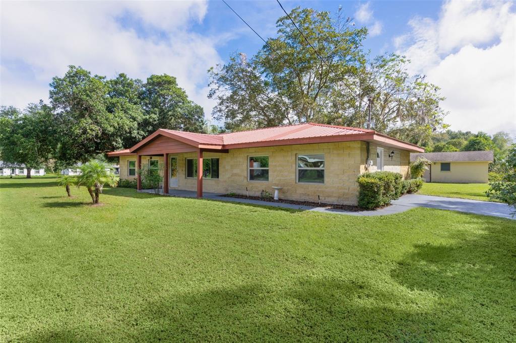 A single-story house with a tan stone facade and a red metal roof — 14635 SE 28TH COURT, SUMMERFIELD, FL