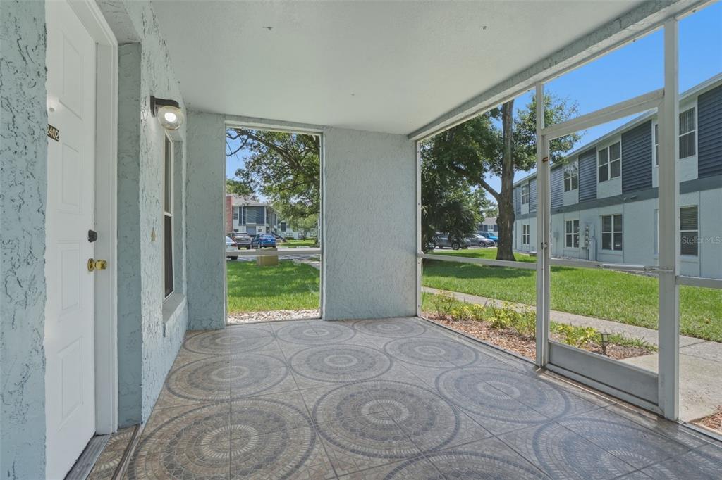 A screened-in porch with patterned tile flooring overlooks a grassy courtyard and apartment buildings — 2402 NORTHLAKE DRIVE UNIT 2402, SANFORD, FL
