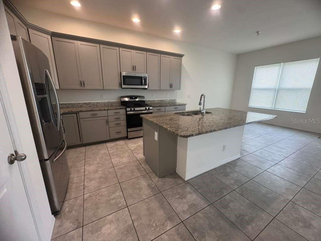 A kitchen with gray cabinets, granite countertops, stainless steel appliances, and a central island — 998 GRAND HILLTOP, APOPKA, FL