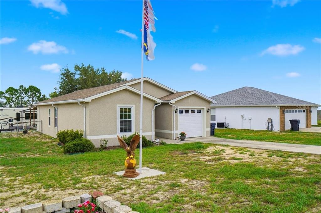 A tan single-story house with a white garage door and a flagpole in the yard — 115 SEMINOLE ROAD, BABSON PARK, FL