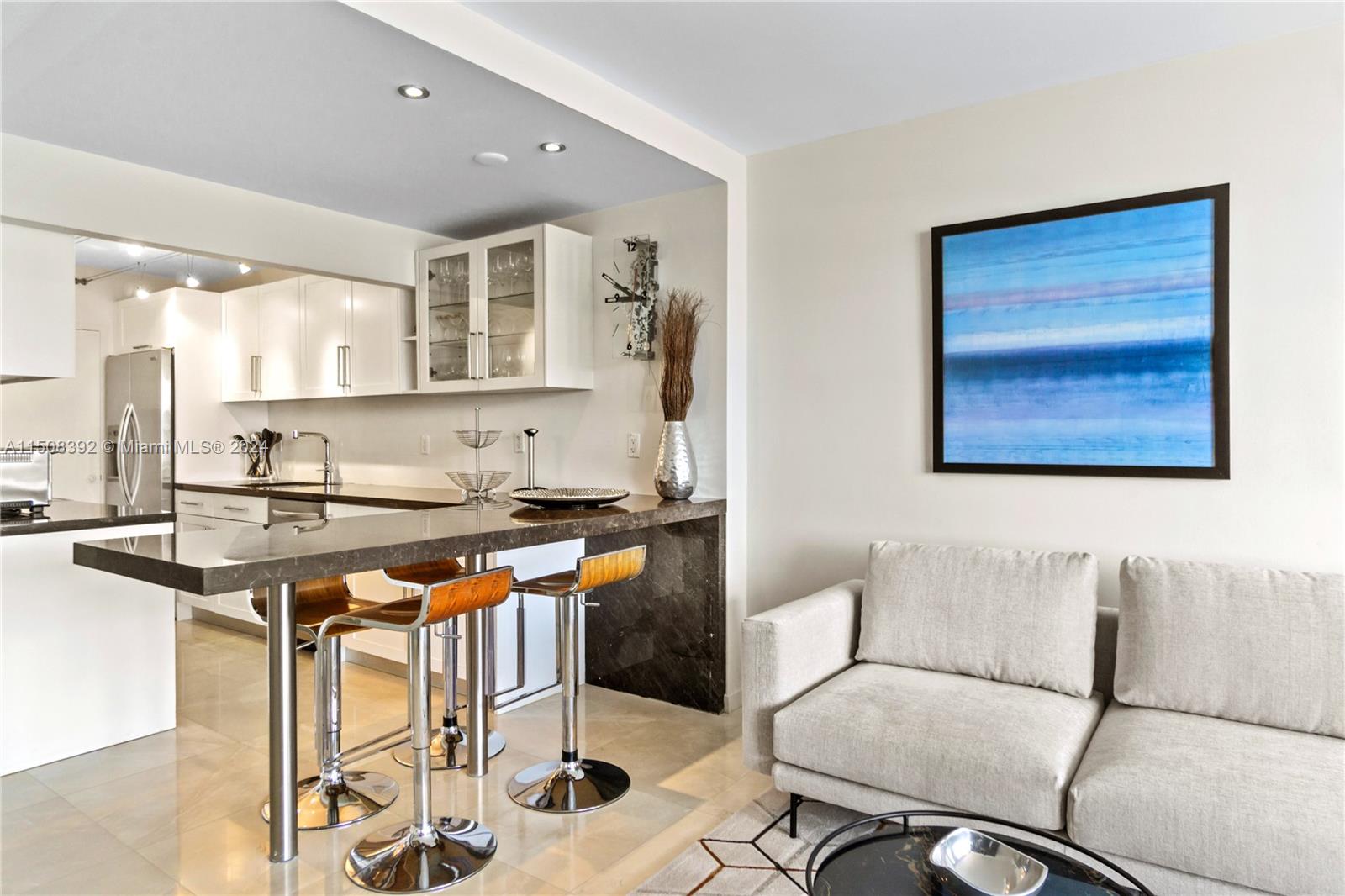 A modern kitchen with a stone breakfast bar and stools sits adjacent to a living area — 100 Lincoln Rd # 1202, Miami Beach FL 33139, MIAMI BEACH, FL