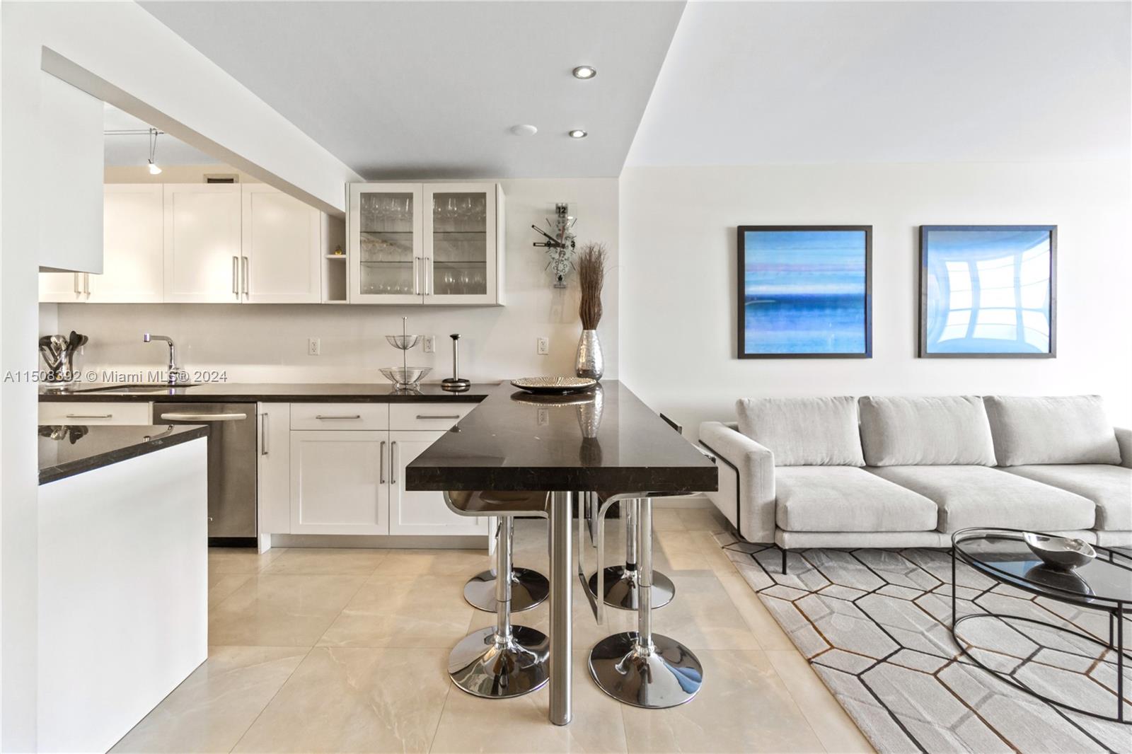 A modern kitchen with white cabinets and a dark countertop island opens to a living area — 100 Lincoln Rd # 1202, Miami Beach FL 33139, MIAMI BEACH, FL
