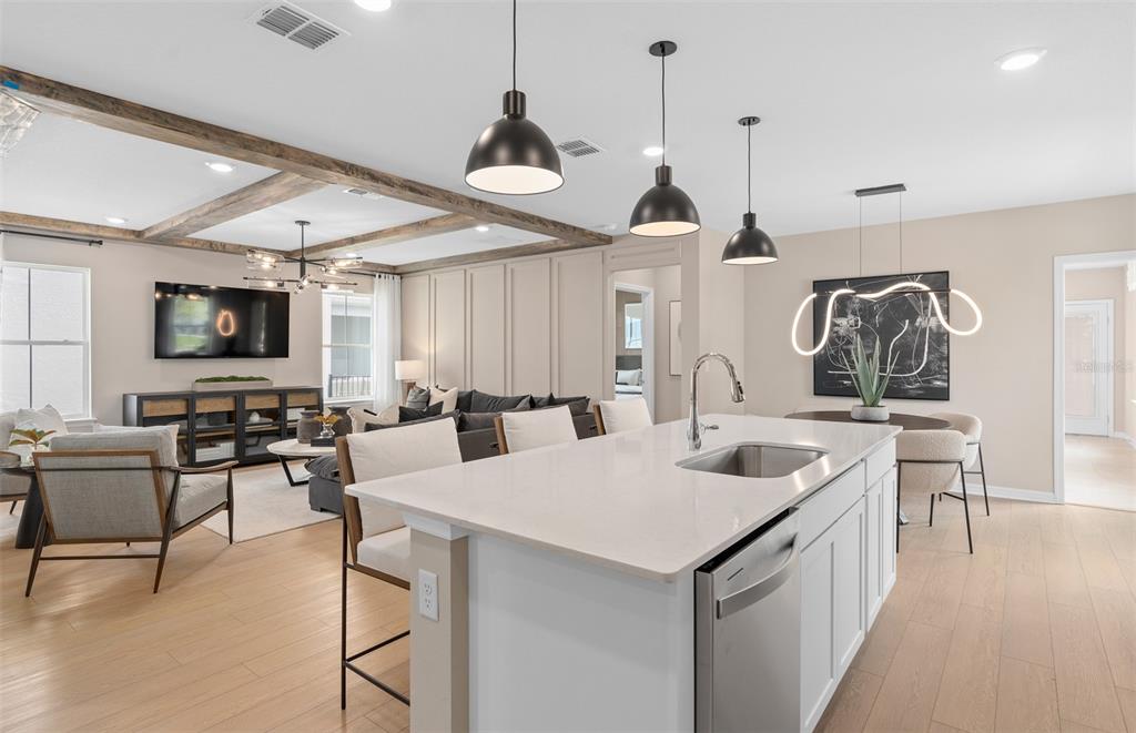 An open-concept kitchen with a white island overlooks a living room with wood ceiling beams — 6902 CREEK FALLS ALLEY, CLERMONT, FL