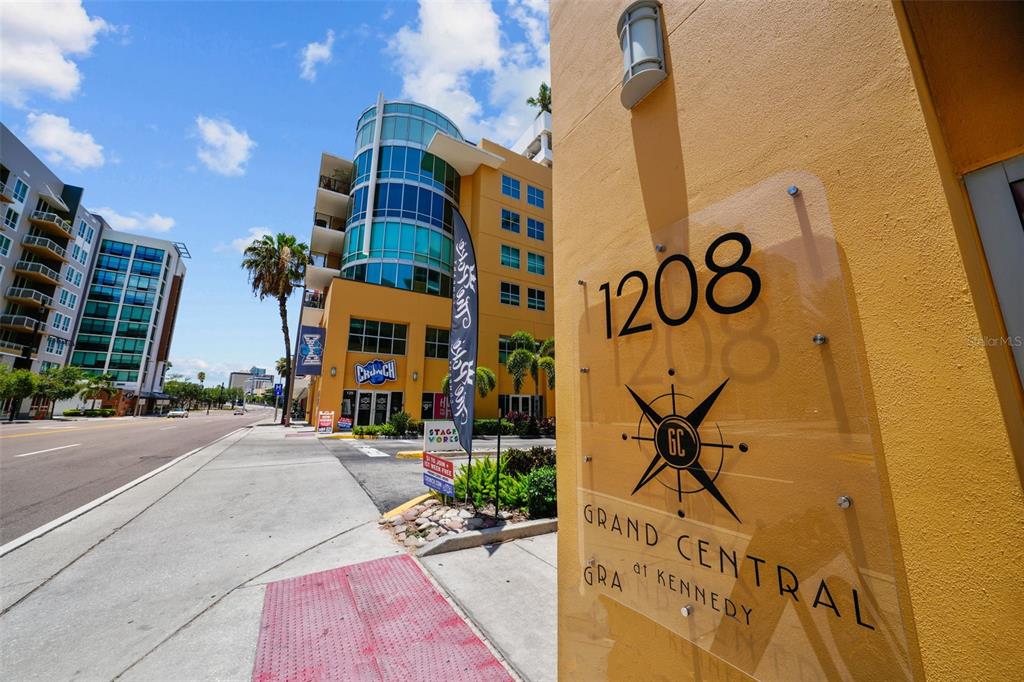 A street-level view shows the exterior of a yellow building with a prominent address sign — 1208 E KENNEDY BOULEVARD UNIT 618, TAMPA, FL
