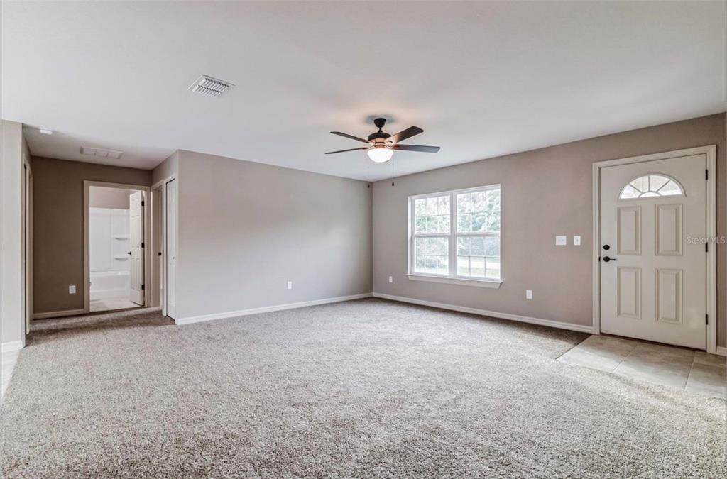 A carpeted room with a ceiling fan, a window, and a door leading outside — 3468 SW 165TH LOOP, OCALA, FL