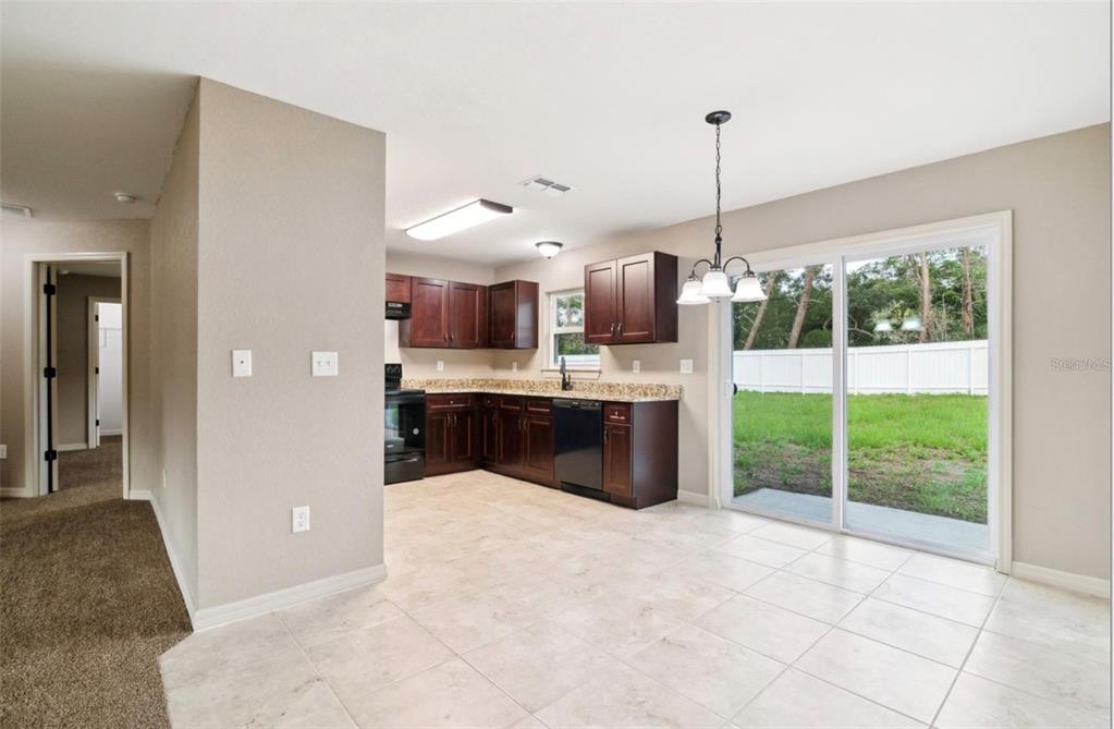 A kitchen with dark wood cabinets, granite countertops, and a sliding glass door to the backyard — 3468 SW 165TH LOOP, OCALA, FL