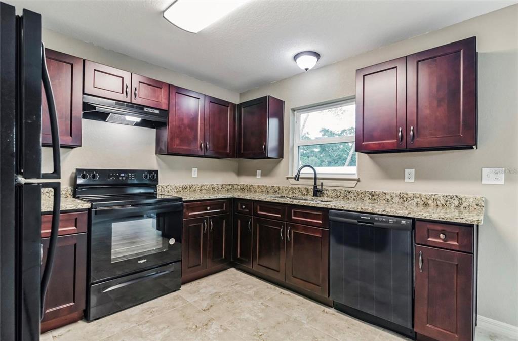 A kitchen features dark wood cabinets, granite countertops, and black appliances — 3468 SW 165TH LOOP, OCALA, FL