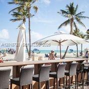 An outdoor bar with wicker stools overlooks a sandy beach with palm trees and umbrellas — N Surf Rd, Hollywood FL 33019, HOLLYWOOD, FL