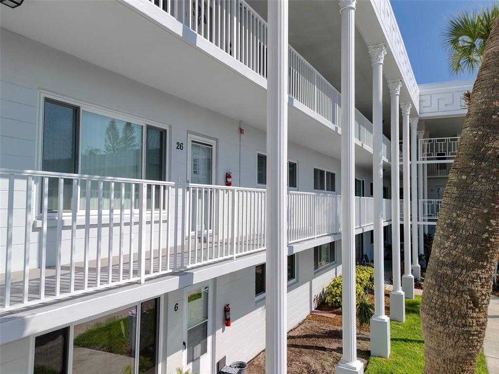 A multi-story white apartment building features exterior walkways with railings and tall decorative columns — 2450 CANADIAN WAY UNIT 26, CLEARWATER, FL