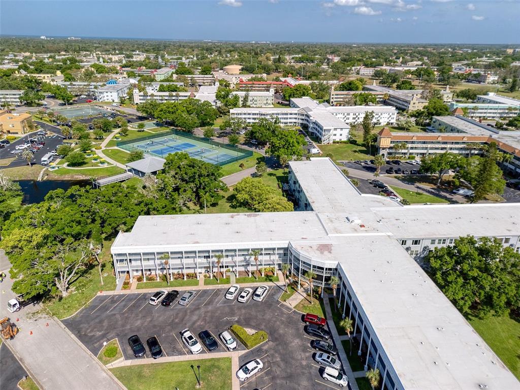 An aerial view shows a large multi-story building with a parking lot and tennis courts — 2450 CANADIAN WAY UNIT 26, CLEARWATER, FL