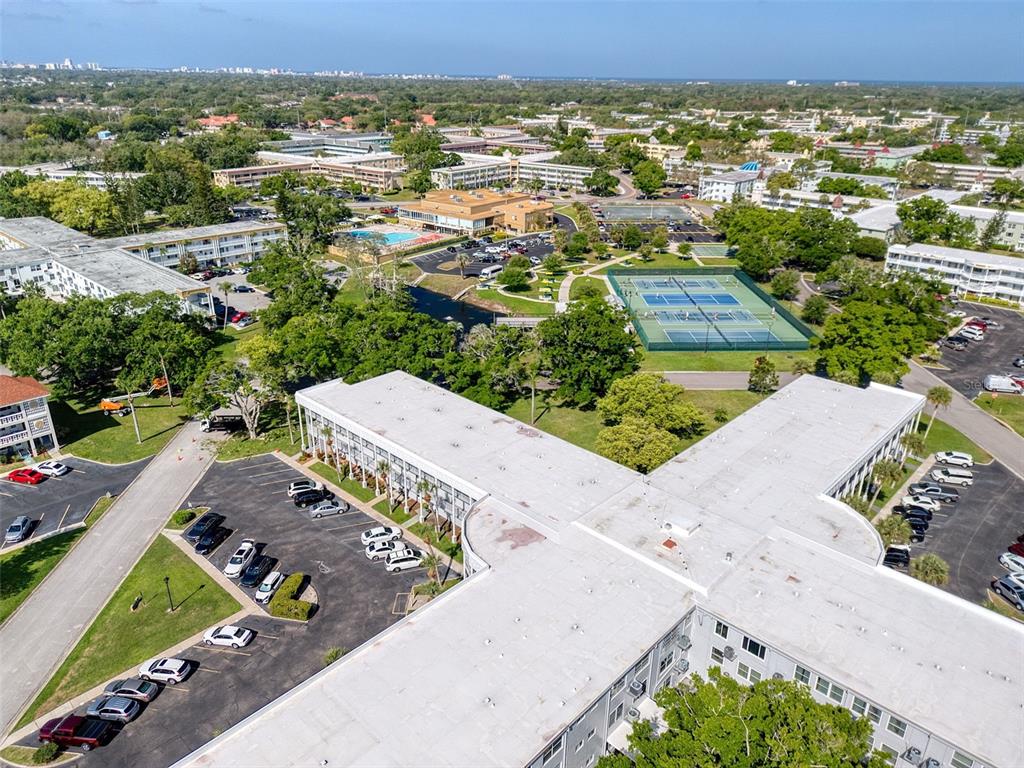 An aerial view shows a multi-story apartment complex with parking lots and tennis courts — 2450 CANADIAN WAY UNIT 26, CLEARWATER, FL