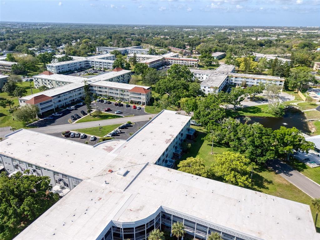An aerial view shows several multi-story apartment buildings with flat roofs surrounded by green trees — 2450 CANADIAN WAY UNIT 26, CLEARWATER, FL