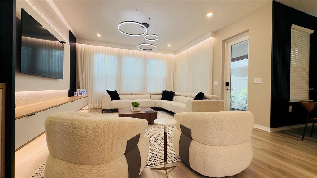 A modern living room features a white sectional sofa, two cream armchairs, and a wall-mounted television — 16192 HONEY HARVEST STREET, WINTER GARDEN, FL