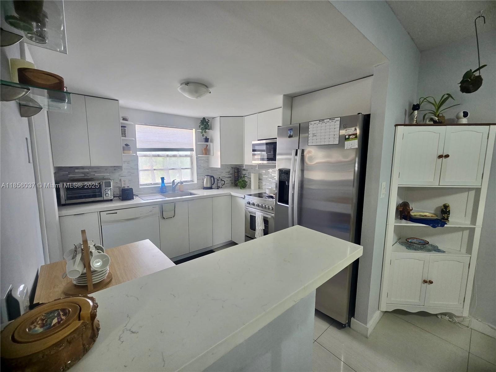 A kitchen features white cabinetry, stainless steel appliances, and a white quartz breakfast bar — 5300 Washington St # U403, Hollywood FL 33021, HOLLYWOOD, FL