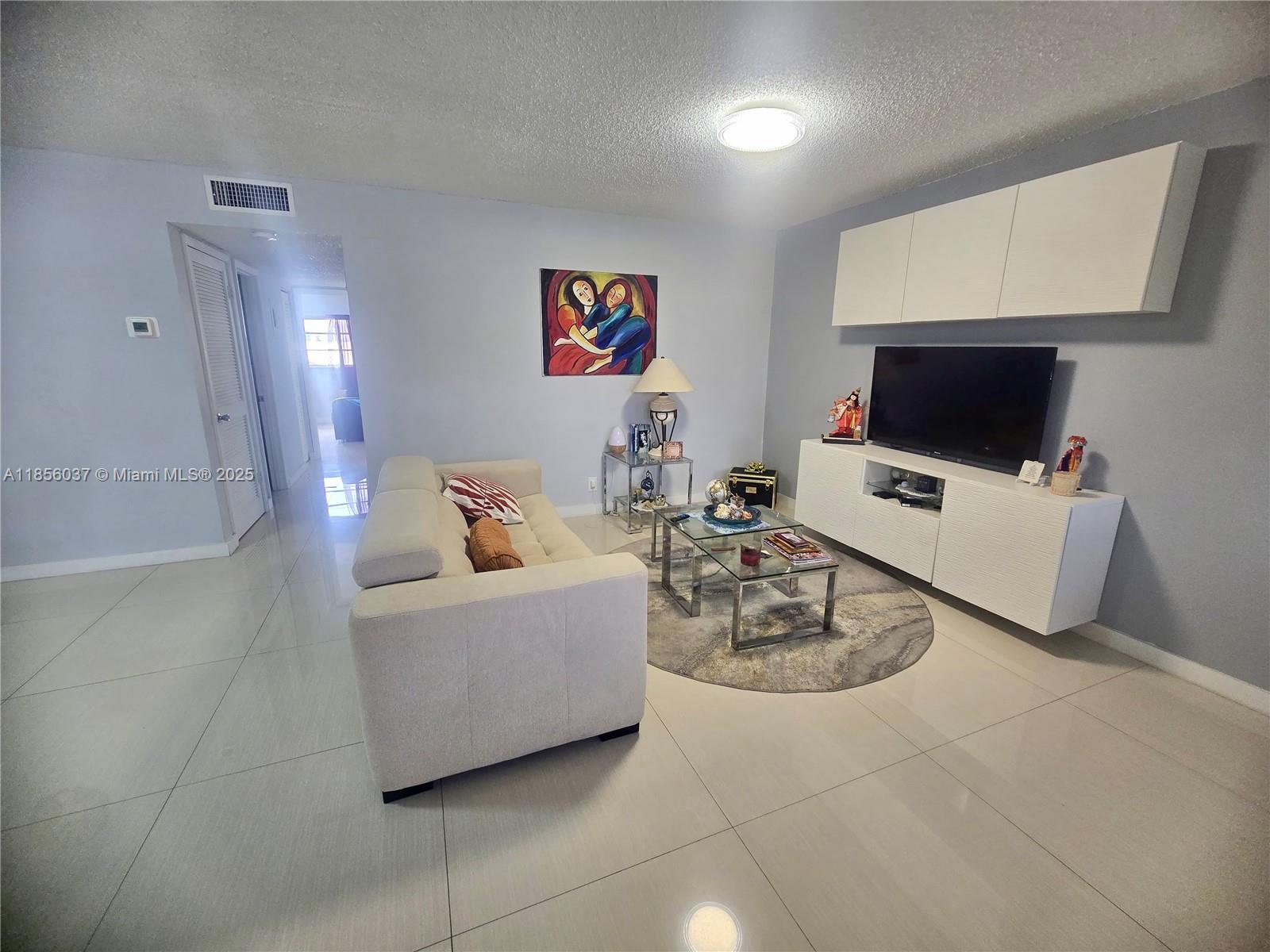 A living room features a beige sofa, a glass coffee table, and a wall-mounted television — 5300 Washington St # U403, Hollywood FL 33021, HOLLYWOOD, FL