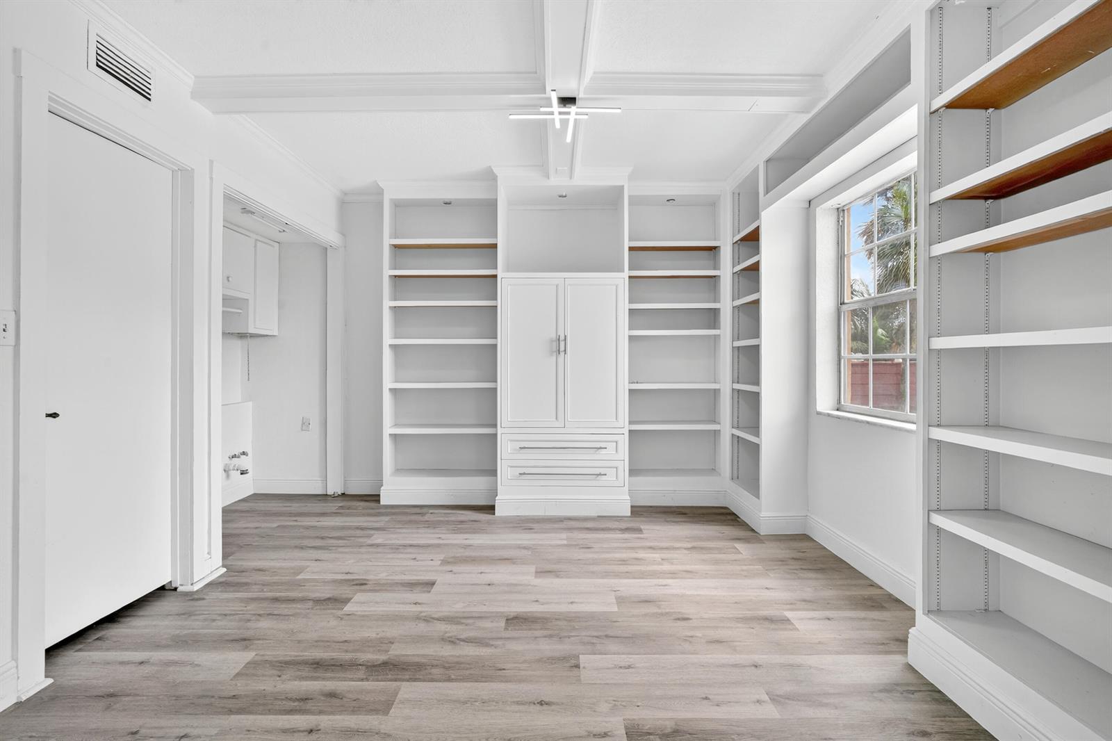 A room with wood-look flooring, white built-in shelving, a central cabinet, and a window — 495 SE 8th Street # 242, Deerfield Beach FL 33441, DEERFIELD BEACH, FL