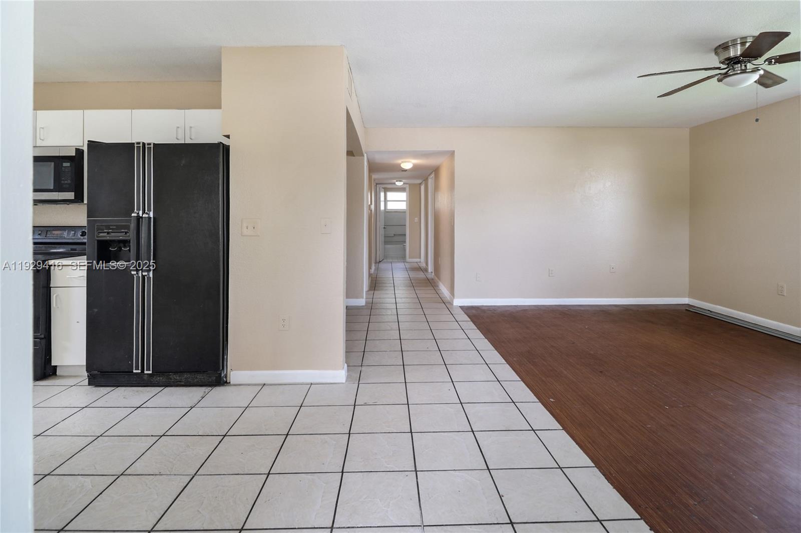 A kitchen with a black refrigerator transitions into a living area with wood-look flooring — 2725 NW 3rd St, Pompano Beach FL 33069, POMPANO BEACH, FL