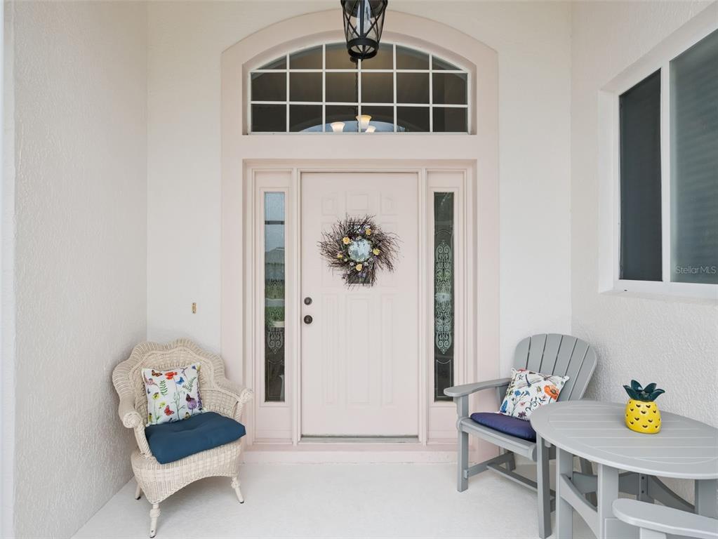 A covered front porch features a light-colored door with sidelights, a transom window, and seating — 21115 ROYAL ST GEORGES LANE, LEESBURG, FL