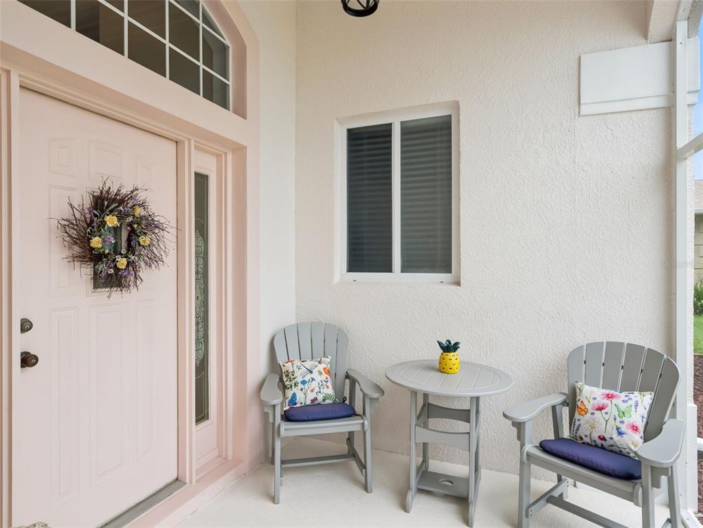 A light-colored front porch features a pink door, two grey chairs, and a small table — 21115 ROYAL ST GEORGES LANE, LEESBURG, FL