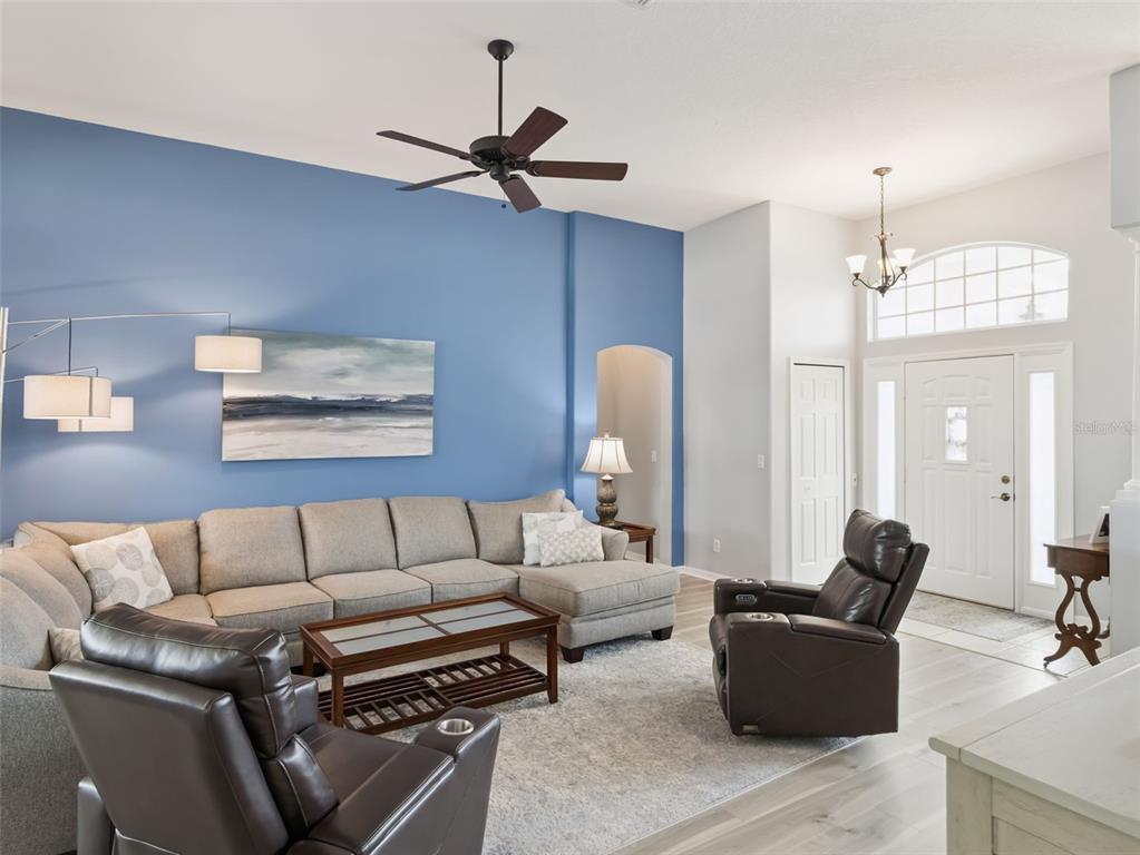A living room features a blue accent wall, a sectional sofa, two recliners, and tile flooring — 21115 ROYAL ST GEORGES LANE, LEESBURG, FL