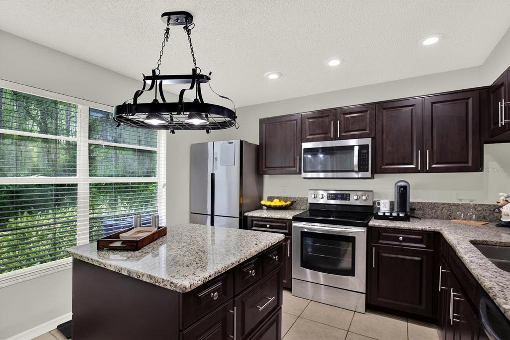 A kitchen features dark wood cabinets, granite countertops, stainless steel appliances, and a central island — 5844 RED CEDAR LANE, TAMPA, FL