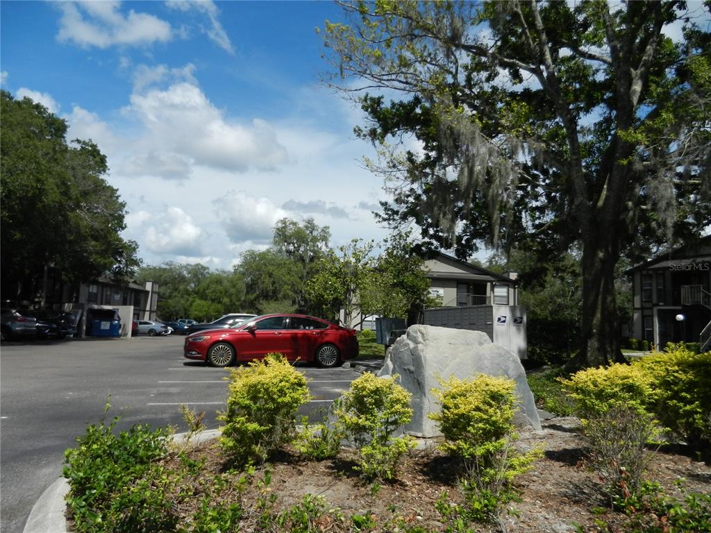 A parking lot with a red sedan, a large boulder, and apartment buildings under trees — 4013 DREAM OAK PL UNIT 103, TAMPA, FL