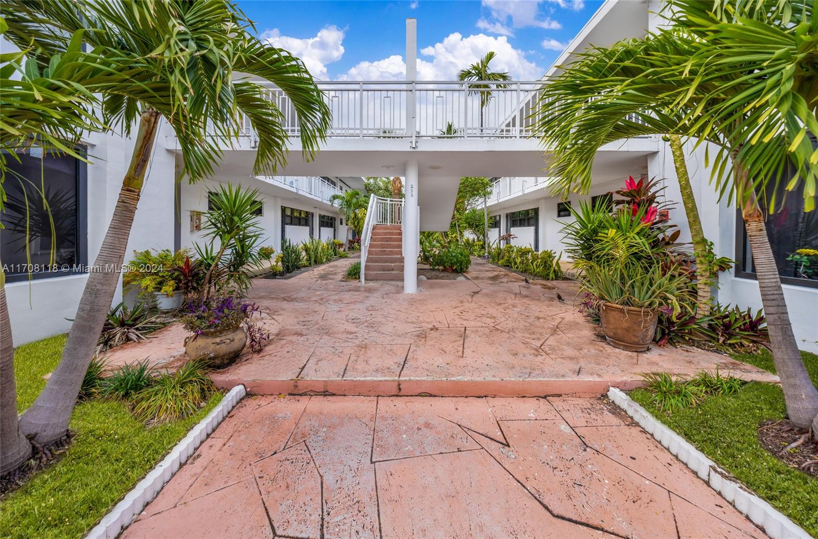 A courtyard with a raised walkway connects two white apartment buildings under a blue sky — 235 78th St, Miami Beach FL 33141, MIAMI BEACH, FL