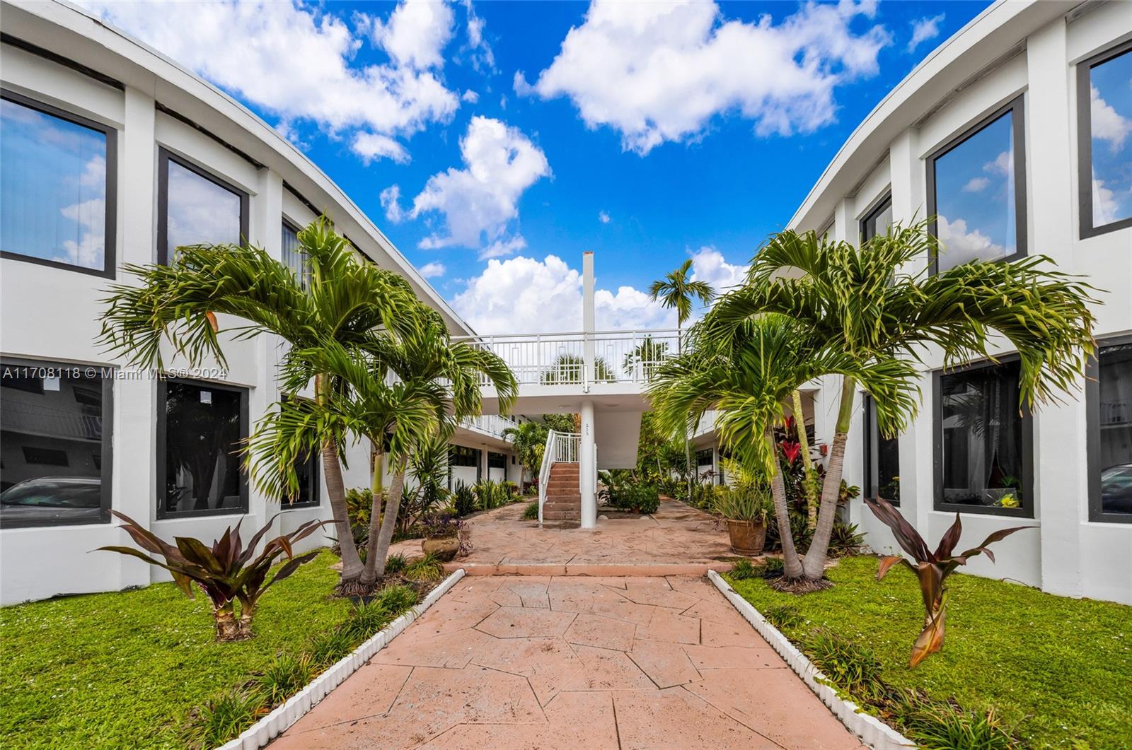 A paved walkway leads between two white apartment buildings with palm trees and landscaping — 235 78th St, Miami Beach FL 33141, MIAMI BEACH, FL
