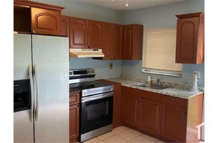 A kitchen features wood cabinets, stainless steel appliances, a light-colored countertop, and tile flooring — 3370 NW 8th Place, Lauderhill FL 33311, LAUDERHILL, FL