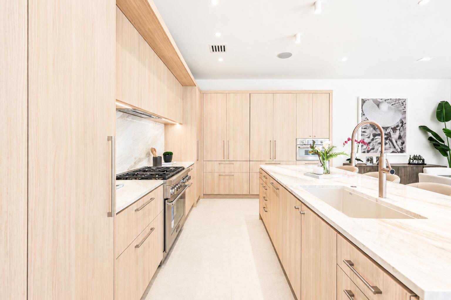 A modern kitchen features light wood cabinetry, marble countertops, and a large central island — 519 SE 4th Avenue, Delray Beach FL 33483, DELRAY BEACH, FL