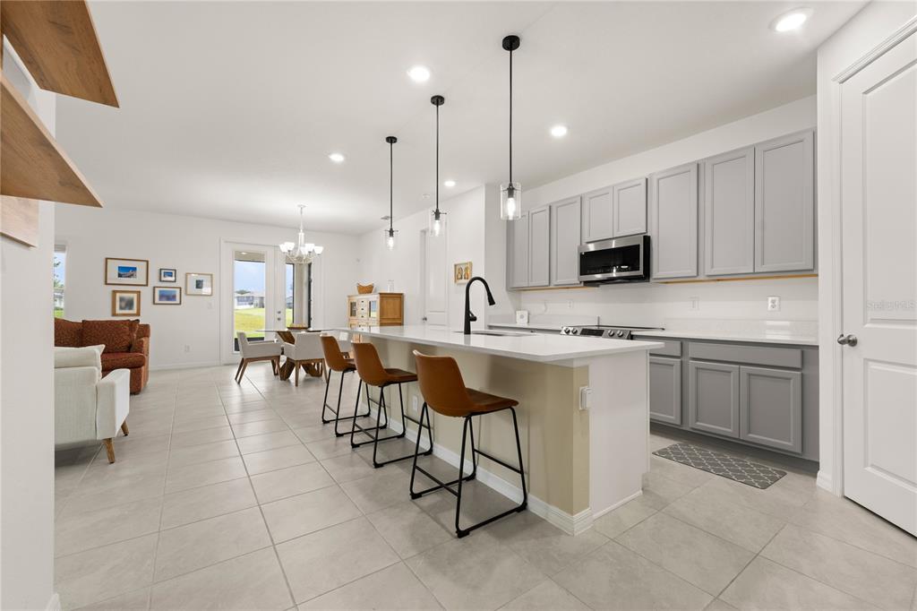 A modern kitchen features gray cabinets, a white island with bar stools, and tile flooring — 1313 STERLING POINTE DRIVE, DELTONA, FL