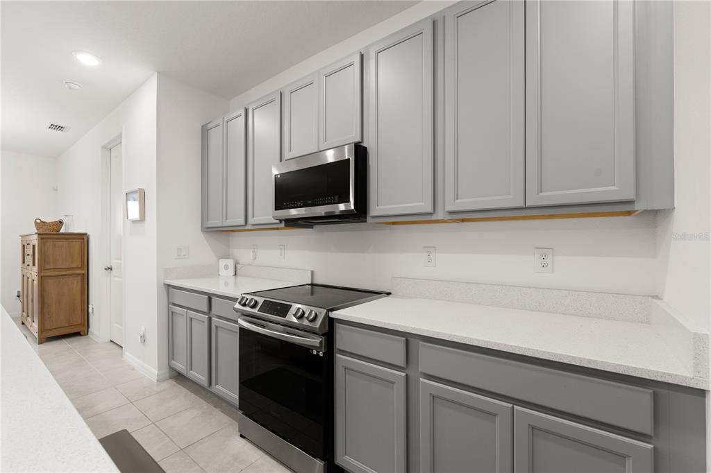 A kitchen features gray cabinets, white countertops, and a stainless steel microwave above the stove — 1313 STERLING POINTE DRIVE, DELTONA, FL