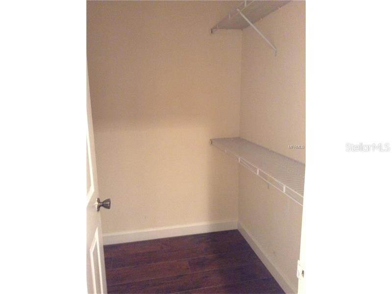 A small walk-in closet features white wire shelving, beige walls, and dark wood-look flooring — 3975 VERSAILLES DRIVE UNIT 3975F, ORLANDO, FL