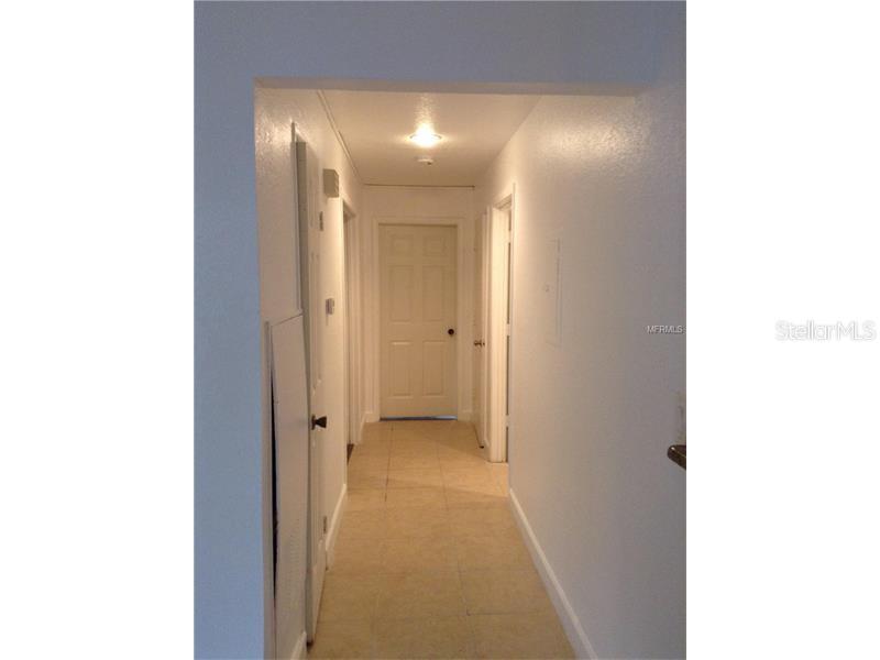 A hallway with white walls, tile flooring, and several closed doors leads to a doorway — 3975 VERSAILLES DRIVE UNIT 3975F, ORLANDO, FL