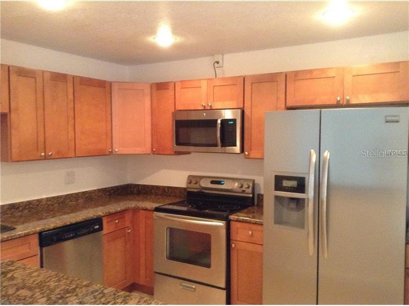 A kitchen features light wood cabinets, stainless steel appliances, and dark granite countertops — 3975 VERSAILLES DRIVE UNIT 3975F, ORLANDO, FL