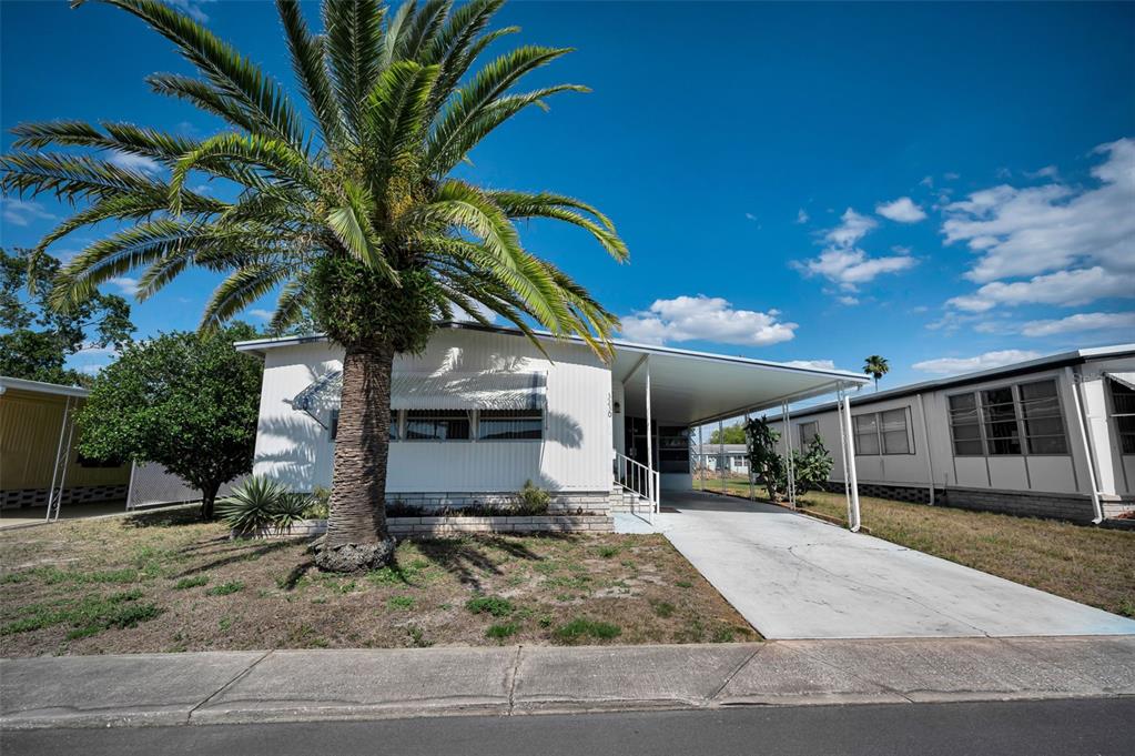 A white mobile home with a palm tree in the front yard and a carport — 3230 LANARK DRIVE, HOLIDAY, FL