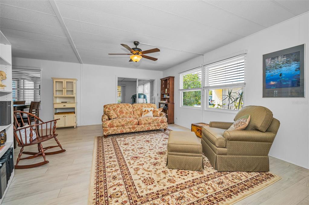 A living room features a floral sofa, an armchair with an ottoman, and light wood flooring — 3230 LANARK DRIVE, HOLIDAY, FL