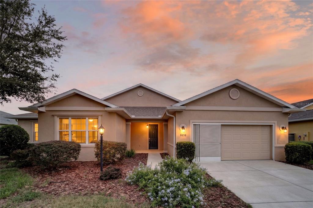 A single-story house with a tan stucco exterior, a two-car garage, and a sunset sky — 9858 SW 90TH STREET, OCALA, FL