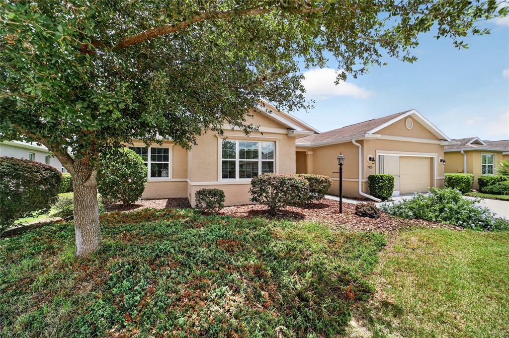 A single-story tan stucco house with a two-car garage and a large front tree — 9858 SW 90TH STREET, OCALA, FL